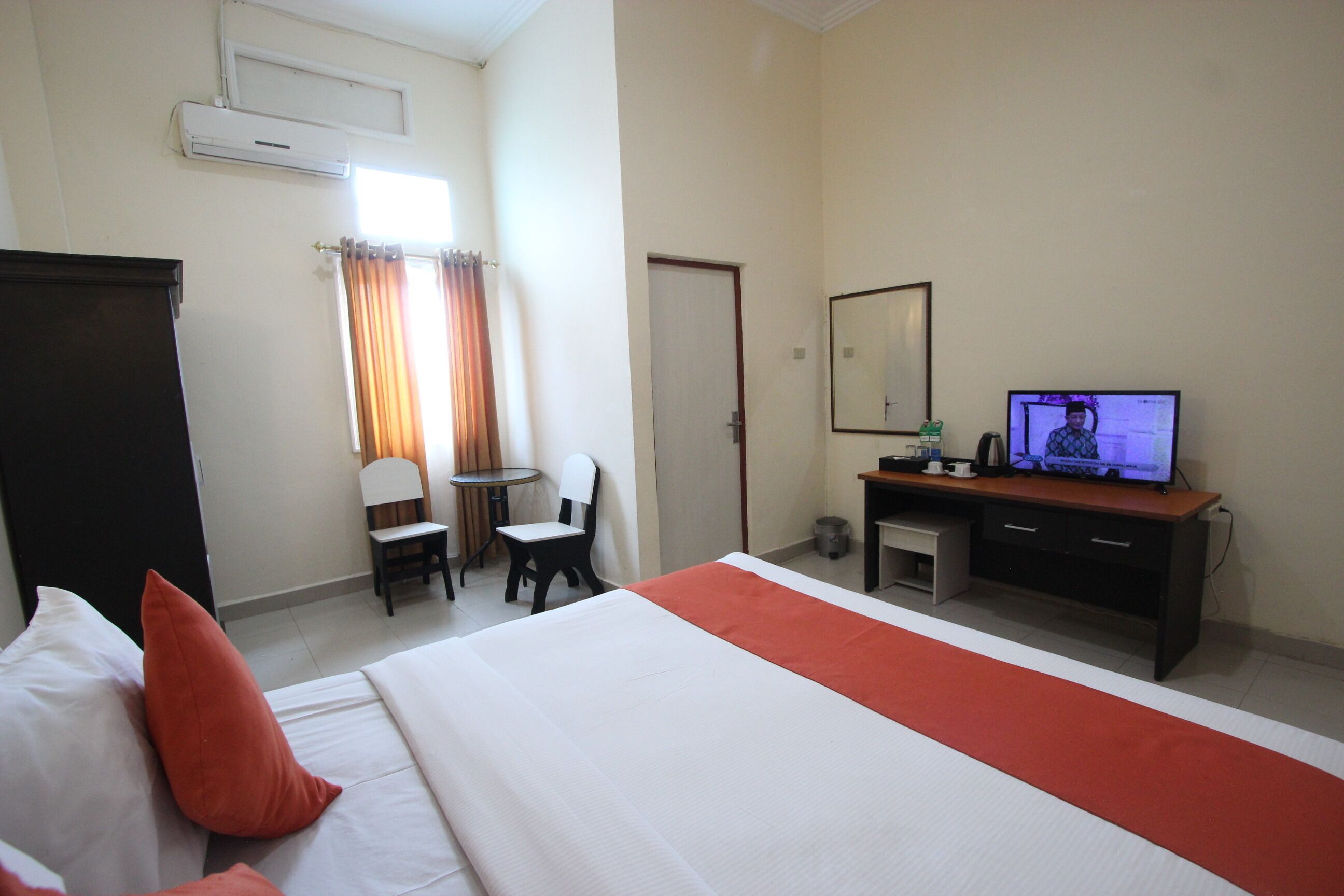 Une chambre d’hôtel équipée d’un lit, d’un bureau, d’une chaise, d’une télévision et d’une fenêtre avec des rideaux.