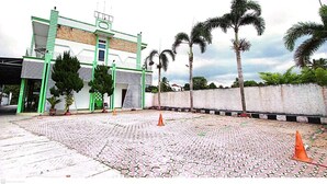 A building with a green and white facade, a paved courtyard with palm trees, and a white wall with black trim. - Yasminstar Hotel (Muntok)