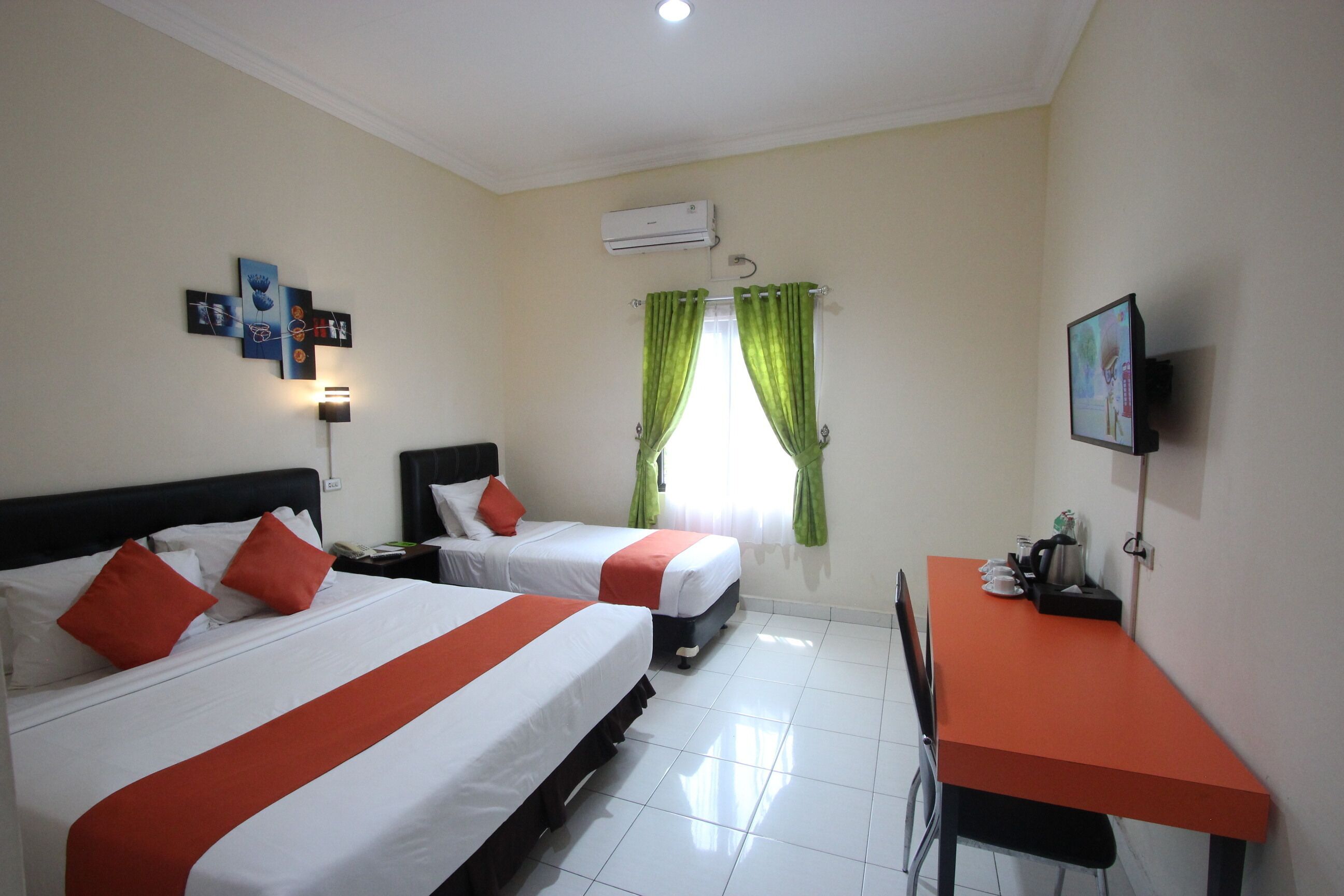 A hotel room with two beds, a desk, a chair, a TV, and an air conditioning unit.