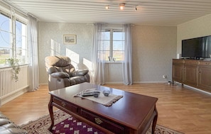 A living room with a leather recliner, a wooden coffee table, a TV stand, and a large window with curtains.