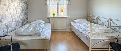 Een slaapzaal met twee eenpersoonsbedden, een radiator, een raam met gordijnen en een muur met behang.