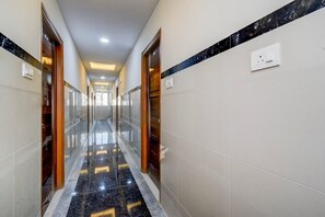 A hallway with a reflective floor, doors, and a light switch on the wall. - Single Room Hotel Lanco Hills (Hyderabad)