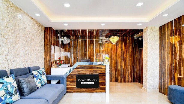 A reception area with a wooden reception desk, a blue sofa, and a marble wall. - Deluxe Rosedale Reliance Guest House (Barasat)