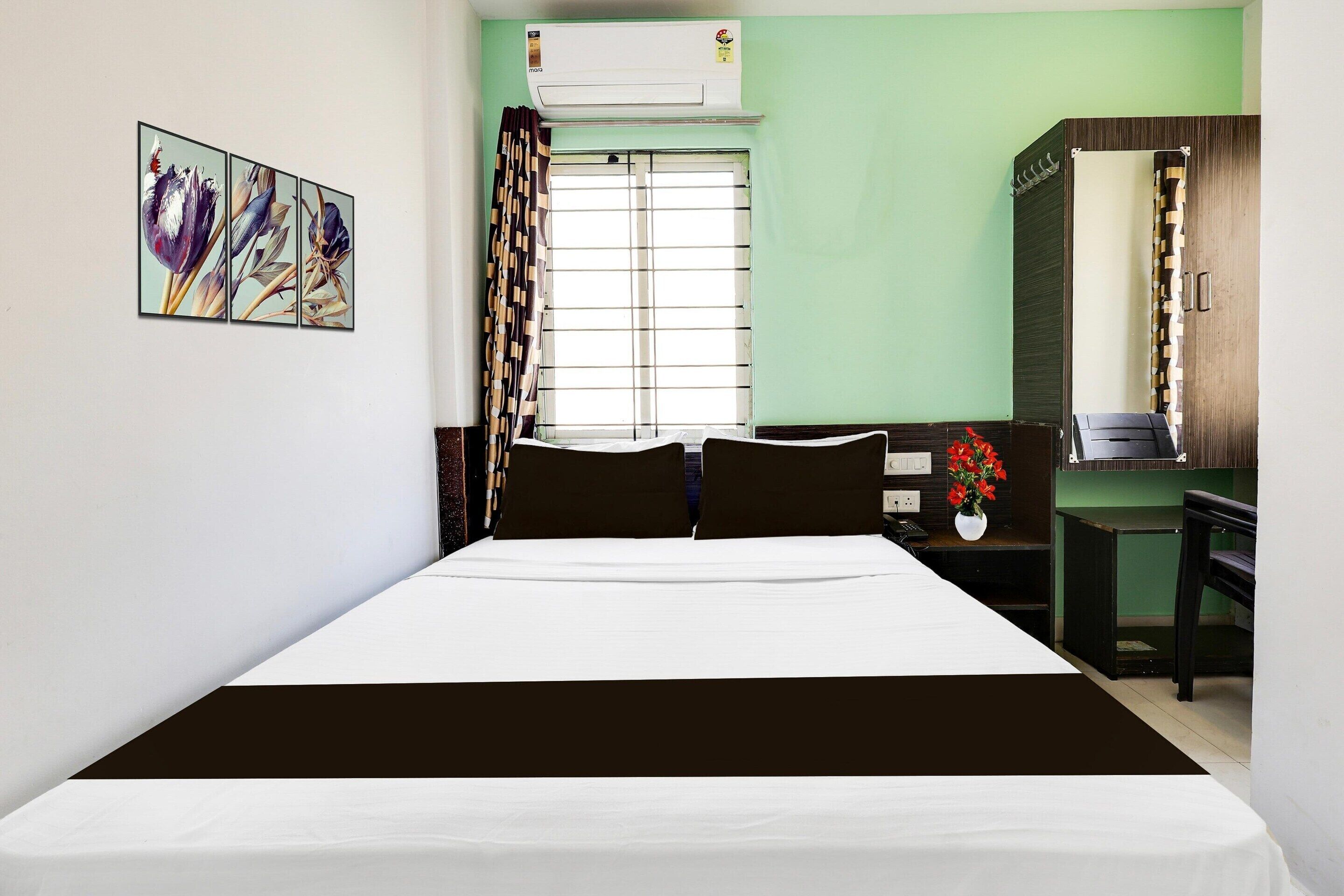 A hotel room with a bed, a desk, a mirror, a window with curtains, and a wall-mounted air conditioner.