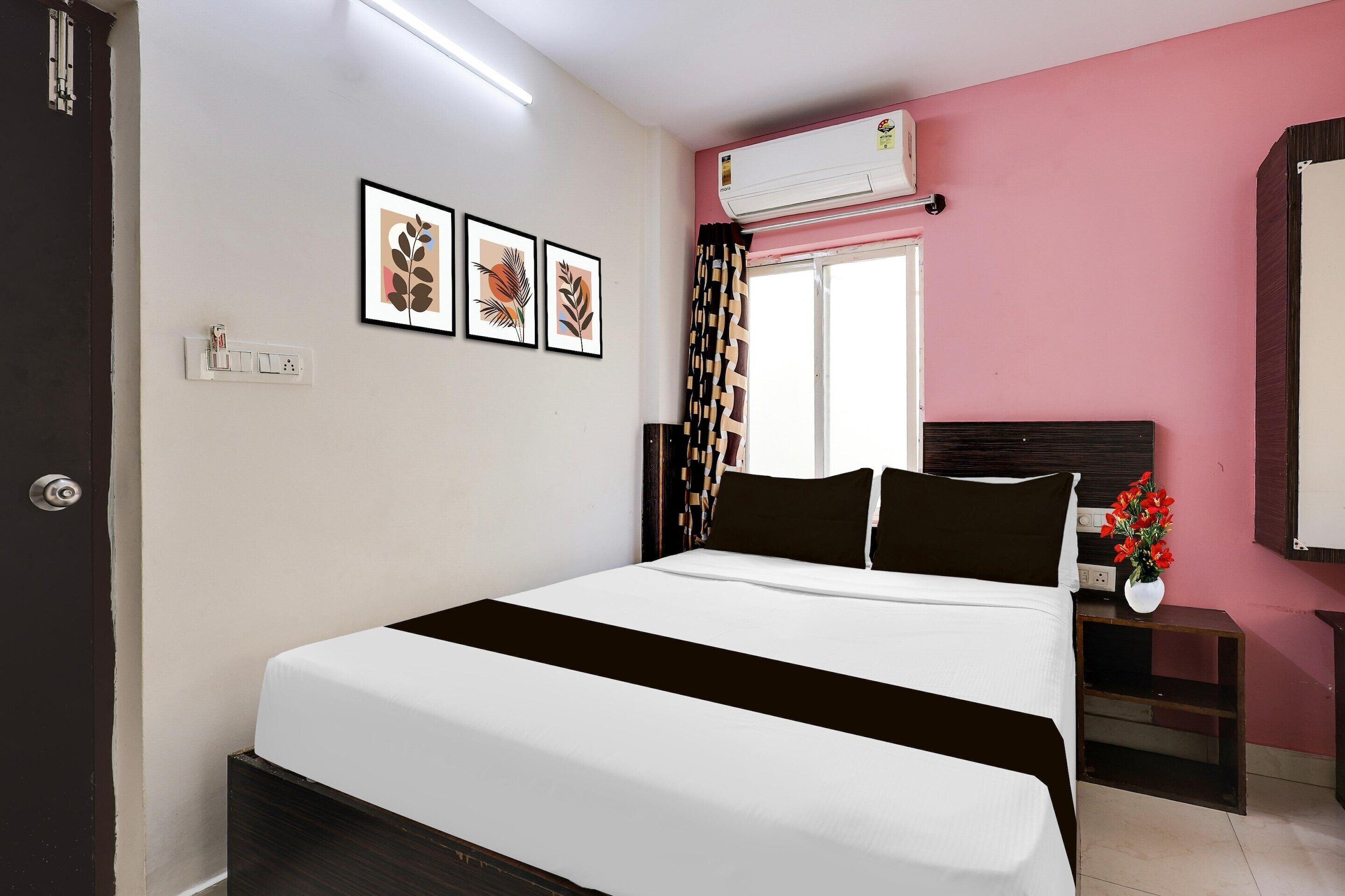 Ein Hotelzimmer mit Bett, Fenster mit gemusterten Vorhängen, Klimaanlage, Wandsteckdose und gerahmten Kunstwerken.