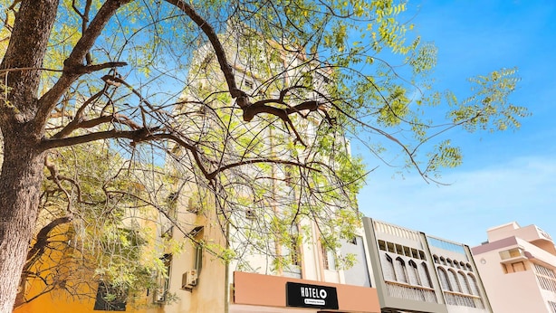 A hotel with a signboard, a tree in front, and a clear blue sky.