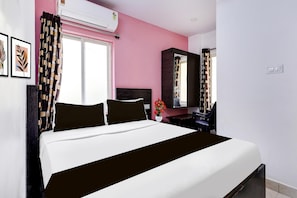 A hotel room with a bed, a desk, a chair, a mirror, and a window with curtains.