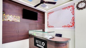 A hotel reception desk with a 'HOTELO' sign, a ceiling fan, a mounted TV, and a decorative wall with a clock.