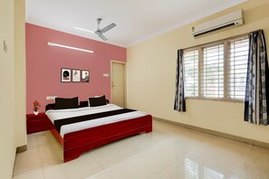 A bedroom with a bed, a ceiling fan, an air conditioner, a window with curtains, and a wall with three framed pictures. - Classic Room Stay Inn Luxury (Kakinada)