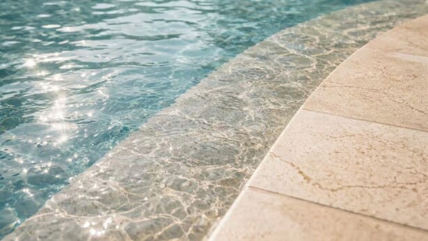 Ein Schwimmbecken mit klarem Wasser, umgeben von Liegestühlen und Sonnenschirmen.