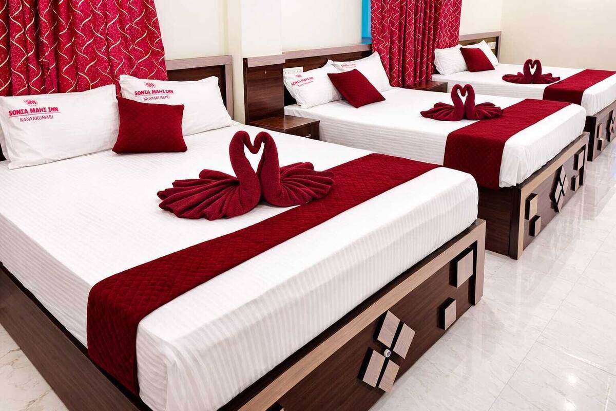 A hotel room with two beds, each with a red blanket and pillows, and a heart-shaped towel decoration.