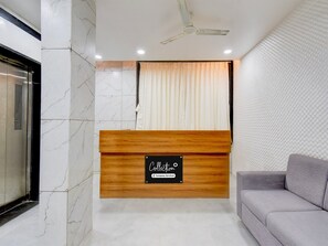 A reception area with a marble wall, a wooden reception desk, a ceiling fan, and a grey sofa. - Super Collection O Aurangabad Shendra Midc (Chhatrapati Sambhajinagar)
