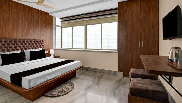 A bedroom with a bed, a ceiling fan, a TV, a window, and a desk with a kettle. - Premium Super Collection O Tollygunge (Kolkata)