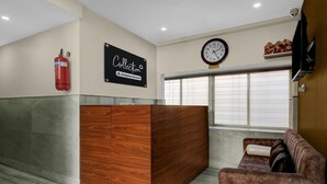 A reception area with a wooden reception desk, a clock, a fire extinguisher, a couch, and a window with blinds. - Premium Super Collection O Tollygunge (Kolkata)