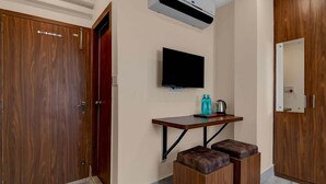 A room with a wooden wardrobe, a mounted TV, a small wooden table with a kettle, and a bench. - Premium Super Collection O Tollygunge (Kolkata)