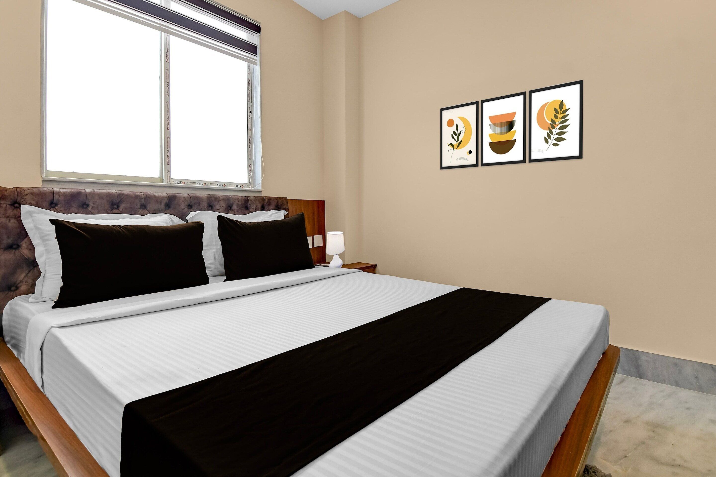 Habitación de hotel con una cama, un ventanal y tres cuadros en la pared.