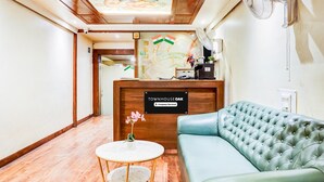 A reception area with a wooden reception desk, a blue sofa, a small round table, and a ceiling fan. - Deluxe Viman Nagar Downtown Cilantro (Pune)