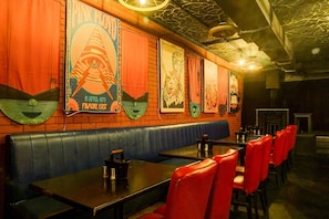 Interior de restaurante con cabinas, sillas rojas y pared de ladrillo decorada con carteles.