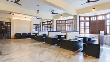 A spacious room with marble flooring, multiple seating areas, ceiling fans, and large windows with wooden frames.