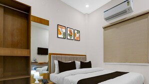 A hotel room with a bed, a bedside table with a lamp, a phone, and a mirror. There are three framed pictures on the wall, and an air conditioning unit above the bed. - Classic With Balcony Dashashwamedh Ghat Varanasi (Varanasi)