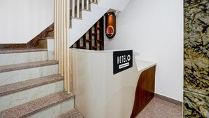 A hotel reception desk with a sign, a staircase with marble steps, and a wall-mounted light fixture. - Classic With Balcony Dashashwamedh Ghat Varanasi (Varanasi)