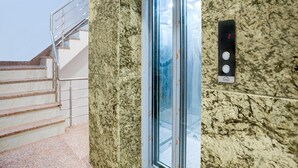 A marble wall with a glass elevator door, a metal handrail, and a control panel with buttons. - Classic With Balcony Dashashwamedh Ghat Varanasi (Varanasi)