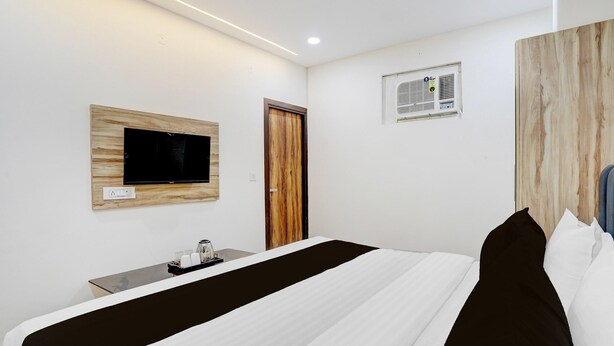 A hotel room with a bed, a TV mounted on a wooden panel, a small table with a tray, and a door. - Saver Singlehotel Lotus (New Delhi)
