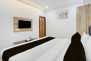 A hotel room with a bed, a TV mounted on a wooden panel, a small table with a tray, and a door. - Saver Singlehotel Lotus (New Delhi)