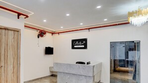A reception desk with a sign, a fan, and a chandelier in a room with tiled flooring and a wooden door. - Saver Singlehotel Lotus (New Delhi)
