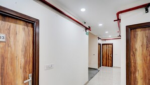 A corridor with wooden doors, a fire exit sign, and a ceiling with red pipes. - Saver Singlehotel Lotus (New Delhi)