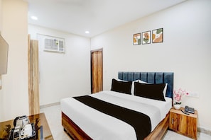 A hotel room with a bed, bedside table, and a wall-mounted air conditioning unit. - Saver Singlehotel Lotus (New Delhi)