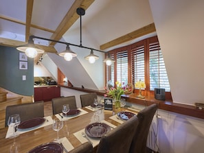 A dining area with a wooden table set for four, a staircase, and a kitchen in the background.