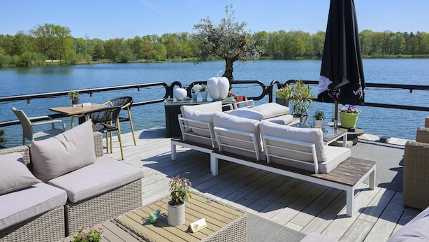 A deck with wicker furniture, a table, and a potted plant. - Beautiful cozy home in a wooded holiday park. (Rekem)