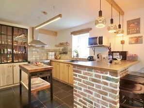 A modern kitchen with a central island, a stove, a microwave, and hanging utensils. - Charming cottage with a lovely terrace & garden (Gimnee)