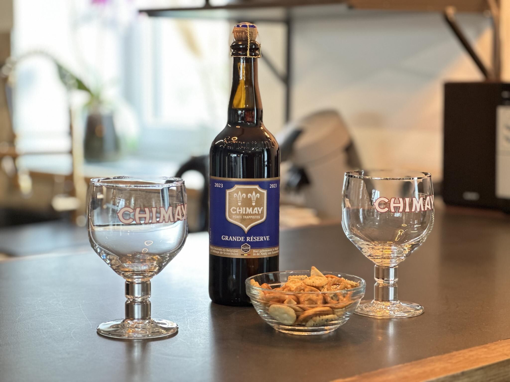 A bottle of Chimap wine, two glasses, and a bowl of snacks on a table.