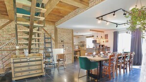 A spacious living area with a staircase, a dining table, and a kitchen in the background. - Charming cottage with a lovely terrace & garden (Gimnee)