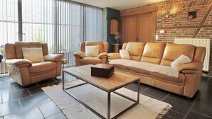A modern living room with leather sofas, a coffee table, and a brick wall. - Charming cottage with a lovely terrace & garden (Gimnee)