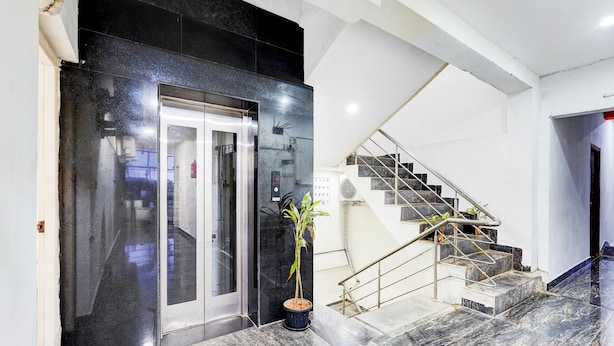 Een moderne lobby met een marmeren vloer, een potplant, een glazen lift en een trap met metalen leuningen.