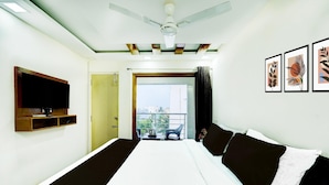 Een hotelkamer met een bed, een aan de muur bevestigde televisie, een balkon met uitzicht en kunstwerken in lijsten aan de wand.