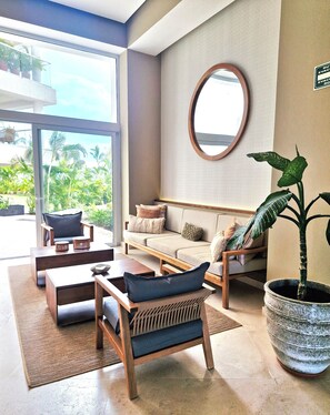 A modern living room with a sofa, chairs, a coffee table, a large mirror, and a potted plant. - Beutiful beachfront apt w/pools/jacuzzi/gym (Puerto Vallarta)