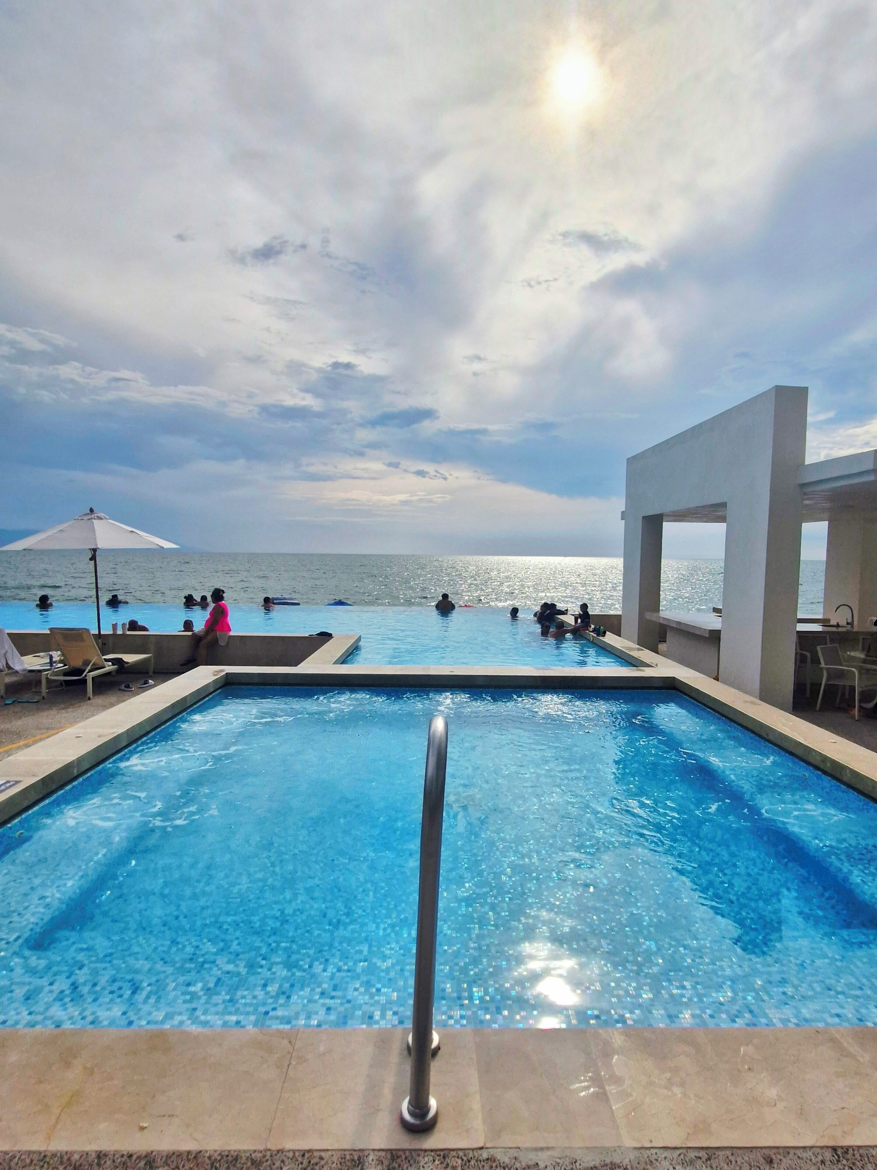Ein Swimmingpool mit Blick auf das Meer, Liegestühle und ein überdachter Bereich.
