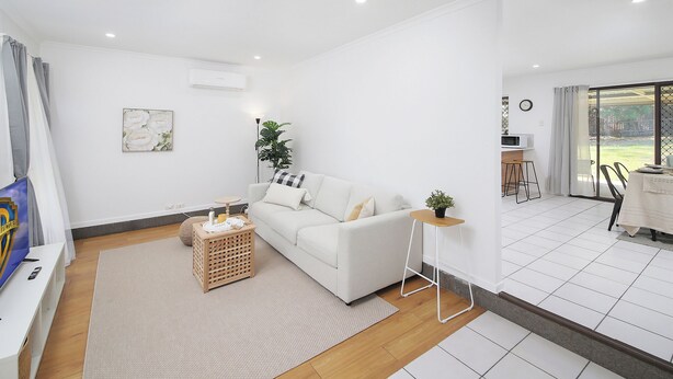 Una sala de estar moderna con un sofá blanco, una mesita auxiliar, una planta y un televisor sobre un mueble.