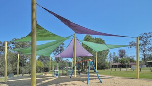 Un parque infantil con columpios y estructuras para escalar, rodeado de árboles y un cielo despejado.