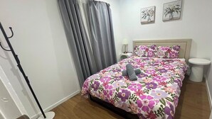 Un dormitorio con una cama, una mesita de noche, una lámpara, un aplique de pie y dos cuadros colgados en la pared.