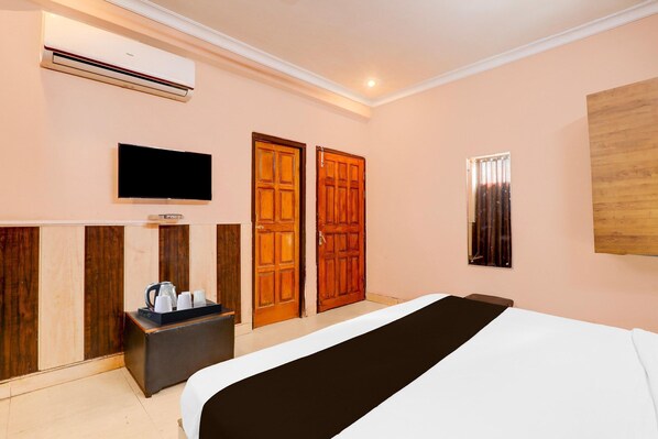 Una habitación de hotel con cama, televisión, puertas de madera y un equipo de aire acondicionado.