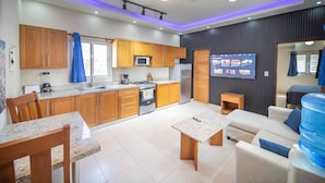 A modern kitchen with wooden cabinets, a microwave, stove, and a dining area with a table and chairs. - Compai Unit 7 Home AC, Wifi, Prime Location (Sosúa)