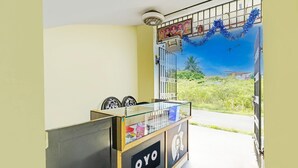 Un mostrador de recepción con encimera de vidrio, un letrero que dice 'OYO' y un mural de paisaje tropical.