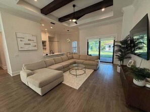 A modern living room with a sectional sofa, a glass coffee table, and a large window offering a view of the outdoors.
