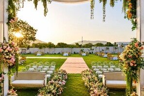 An outdoor wedding venue with a paved aisle, white chairs, and floral arrangements. - Treat Imperial Hridhaan Udaipur (Udaipur)