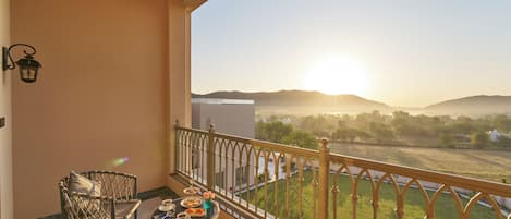 A balcony with wicker furniture, a table with food and drinks, and a view of a landscape with hills and a clear sky.